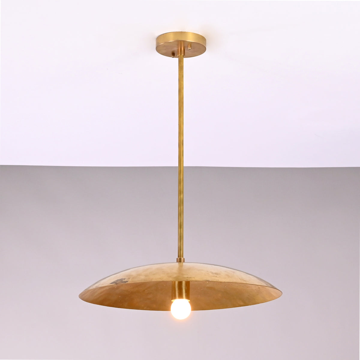 Front view of Aurelia Petite Saucer Pendant Light with slim downrod and softly glowing single bulb.