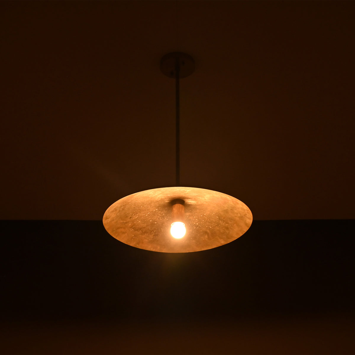 Aurelia Petite Saucer Pendant Light glowing in a dark setting with warm focused downward illumination.