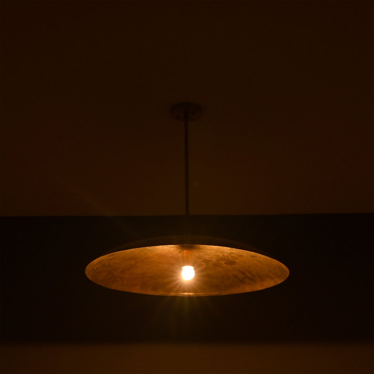 Aurelia Saucer Pendant Light glowing in a dark setting with soft downward ambient light effect.