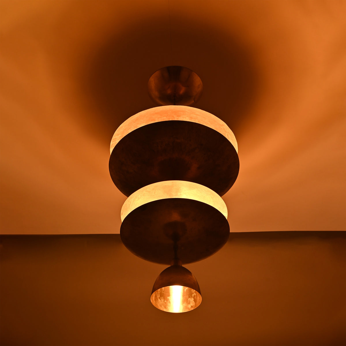 Low angle view of Aurelia Tiered Disc Chandelier with illuminated stacked discs and pendant-style lower shade.