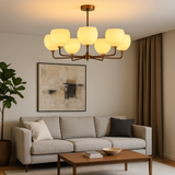 Modern brass chandelier with eight frosted glass globe lights, hanging in a cozy living room with neutral-toned decor