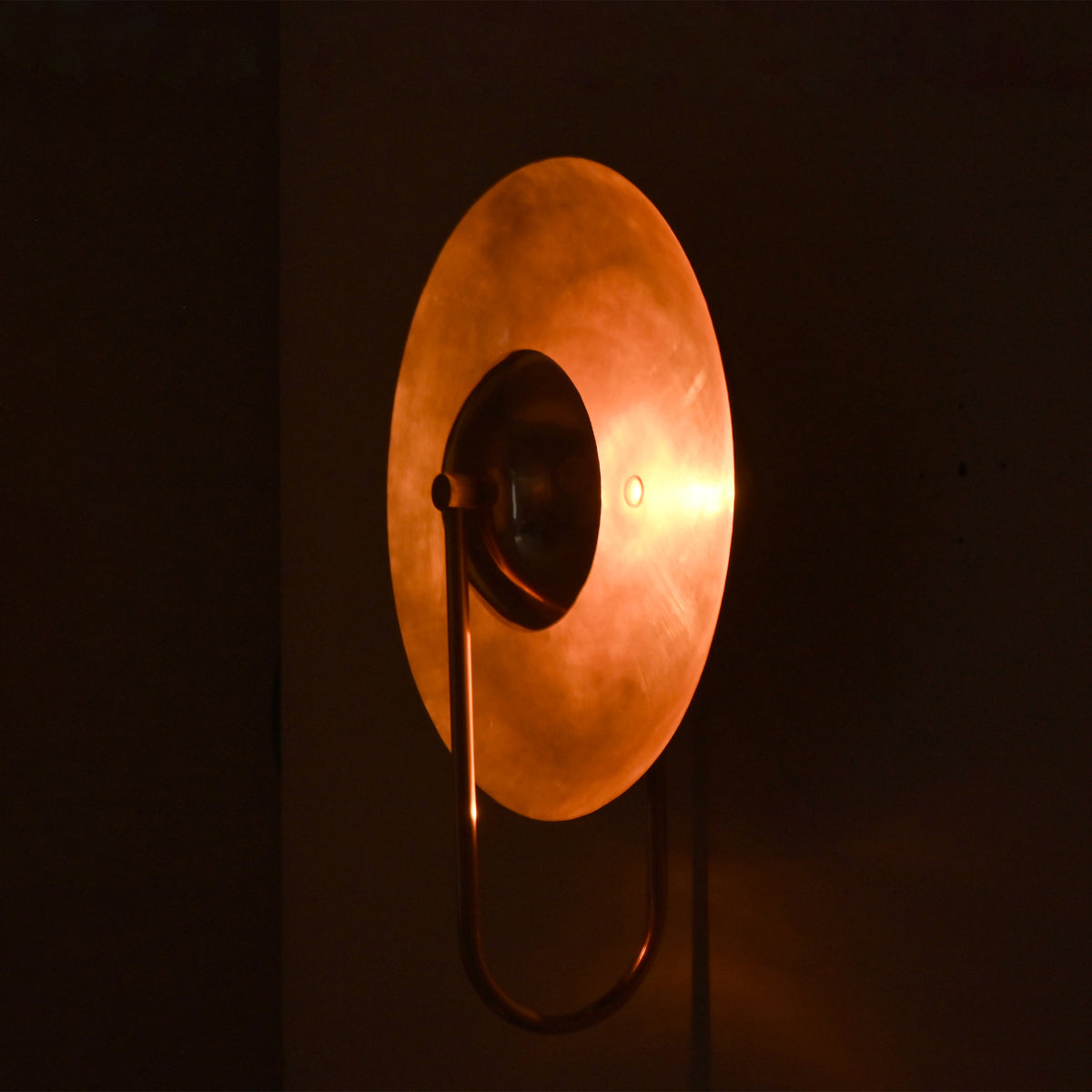 Perspective view of the Aurora modern copper halo wall sconce displaying its warm ambient glow and contemporary circular metal reflector.
