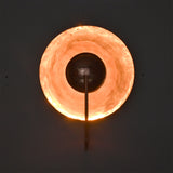 Illuminated front view of the Aurora modern copper halo wall sconce casting a warm indirect glow through its polished circular reflector.