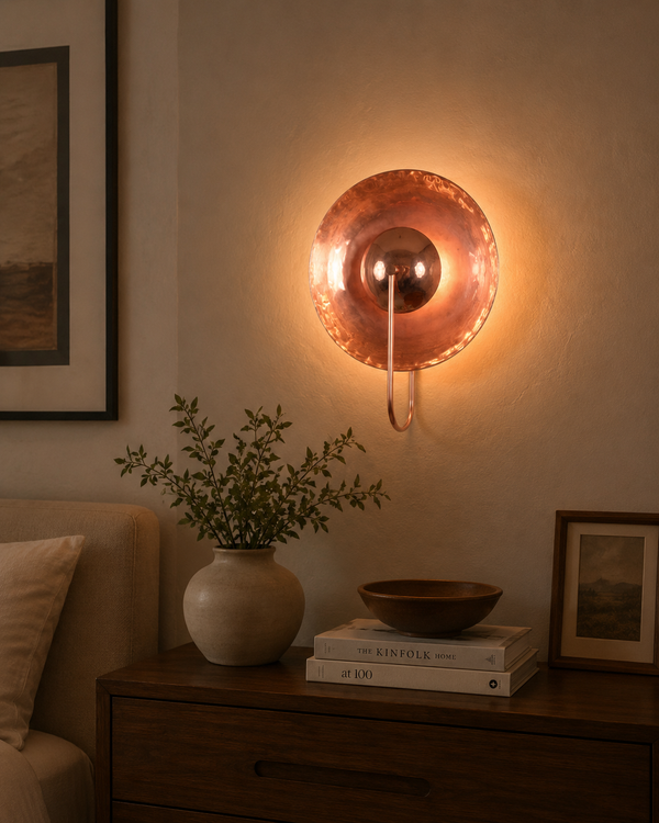Styled interior view of the Aurora modern copper halo wall sconce installed above a wooden console, creating warm ambient lighting in a modern living space.