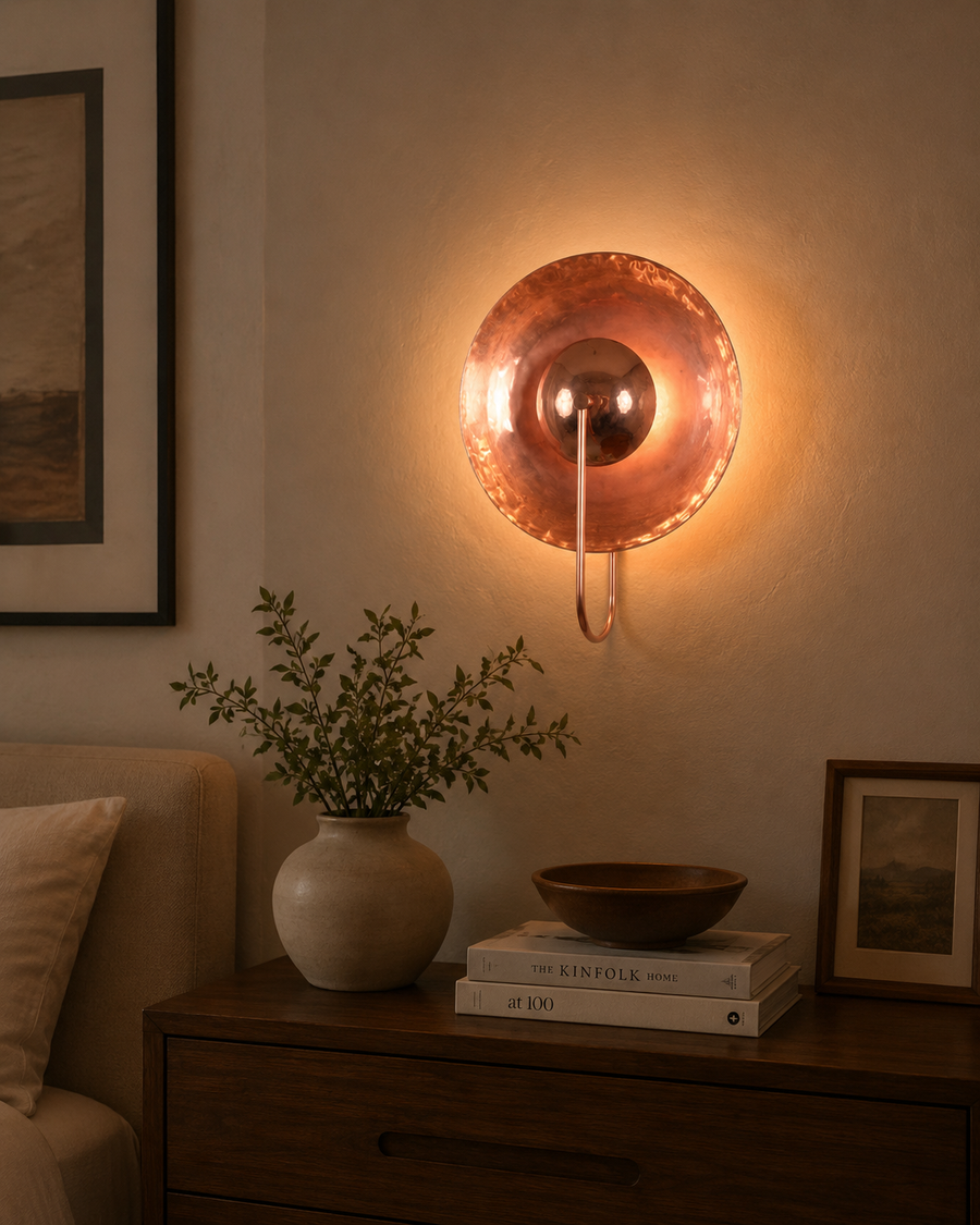 Styled interior view of the Aurora modern copper halo wall sconce installed above a wooden console, creating warm ambient lighting in a modern living space.