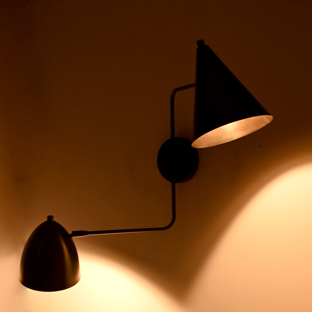 Illuminated front view of the Aurora modern dual shade wall sconce casting warm upward and downward ambient light through dual matte black tapered metal shades.