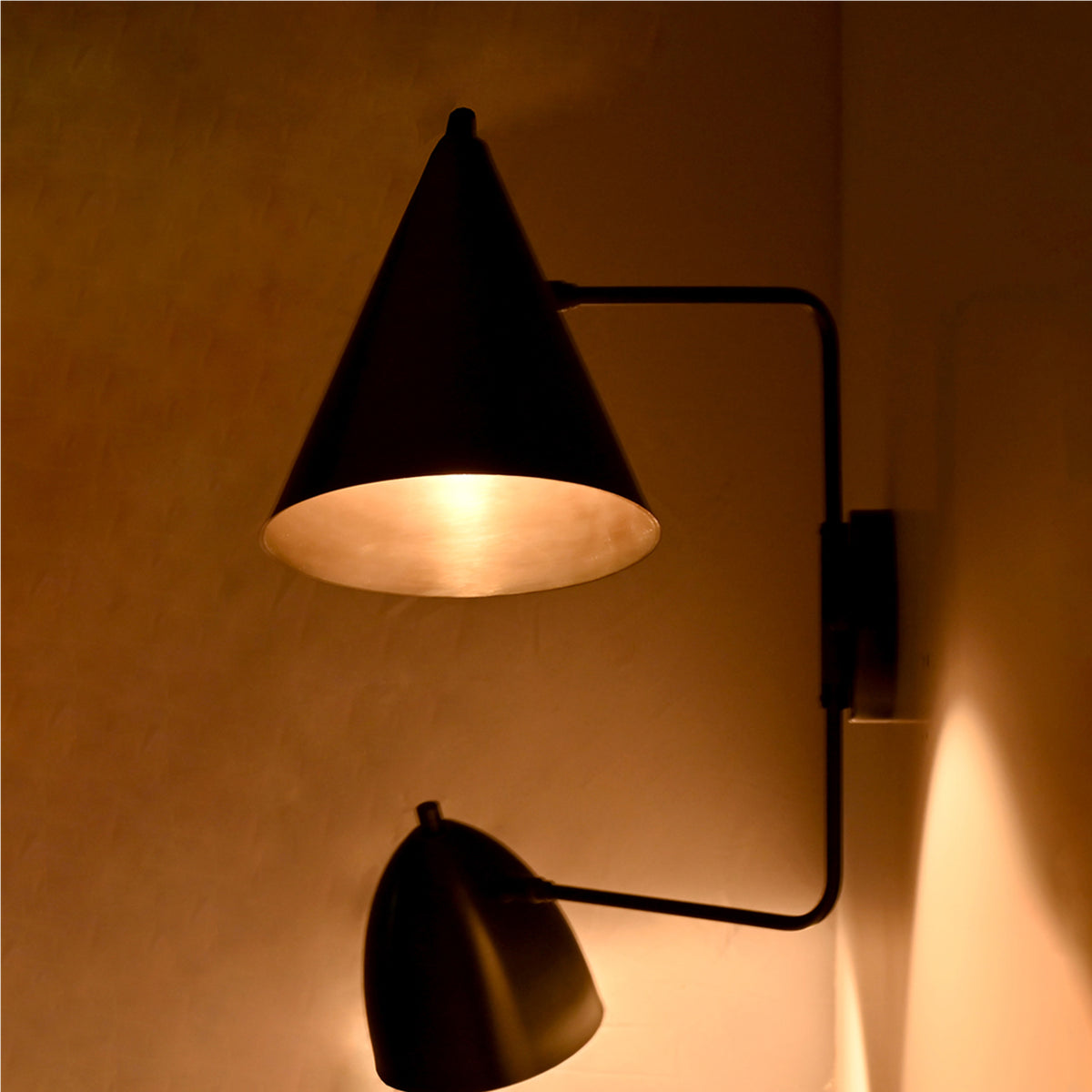 Side view of the Aurora modern dual shade wall sconce illuminated with warm ambient lighting, featuring handcrafted matte black tapered shades and a sleek architectural frame.