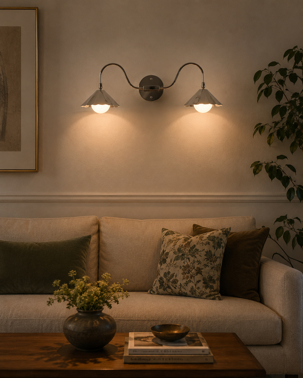 Aurora modern polished nickel double wall sconce installed above a living room sofa, providing warm ambient illumination with dual fluted shades and frosted globe diffusers.