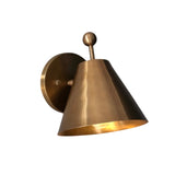 Illuminated Aurora satin brass tapered wall sconce casting a warm downward glow from its modern cone-shaped shade.