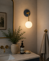 Aurora opal globe wall sconce with brass stem installed beside a bathroom vanity mirror with warm ambient lighting