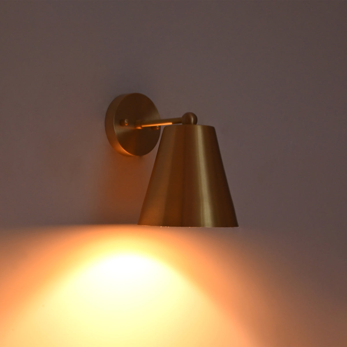 Angled illuminated view of the Aurora satin brass tapered wall sconce highlighting the warm focused light and elegant tapered metal shade.