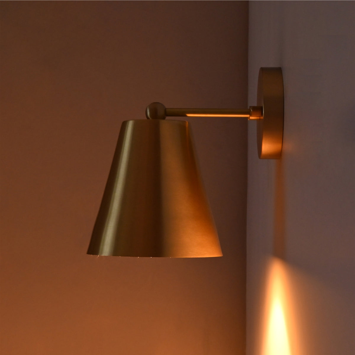 Side view of the Aurora satin brass tapered wall sconce displaying its warm ambient illumination and sleek satin brass finish.