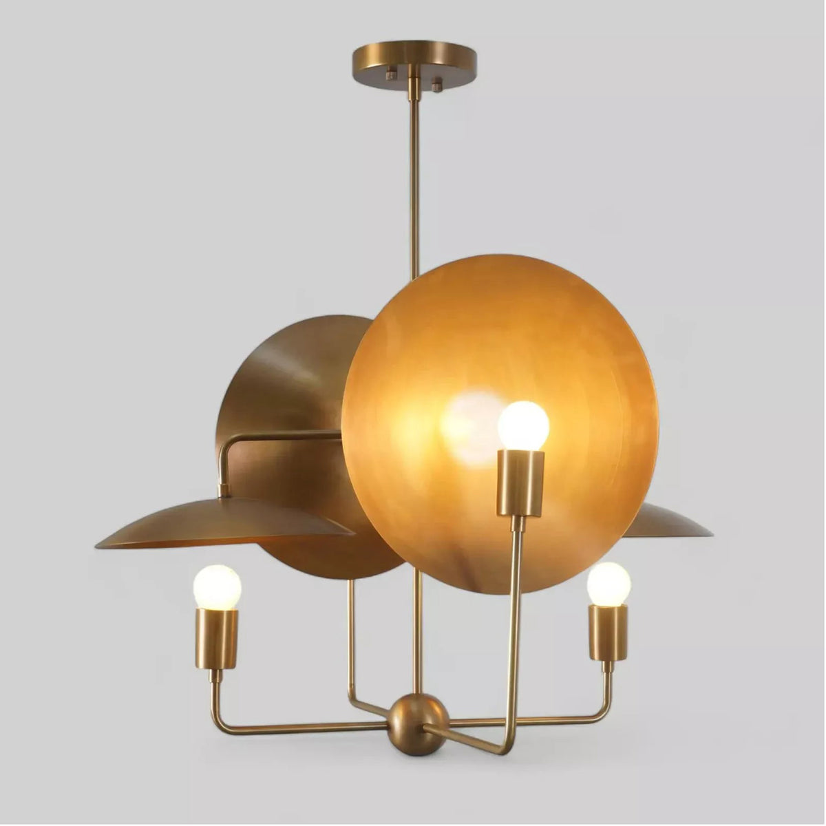 Angled view of the Aurora Sculptural Disc Chandelier featuring four exposed globe bulbs, handcrafted metal disc reflectors, and a warm brass finish illuminated.