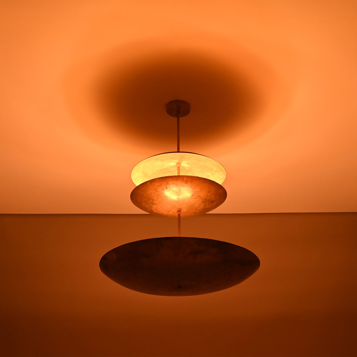 Aurora Triple Saucer Chandelier glowing warmly in low light with dramatic ambient ceiling illumination.