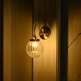 Angled nighttime view of Austin brass wall sconce with a curved gooseneck arm and illuminated fluted glass globe creating a warm ambient glow.