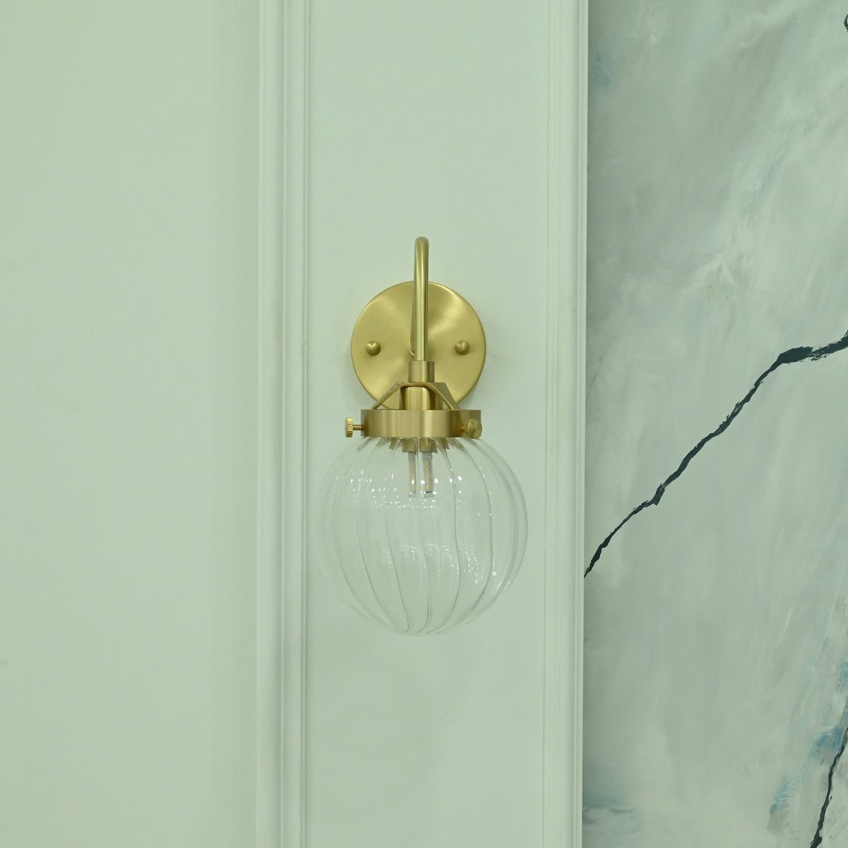 Austin single-light wall sconce featuring a brass finish, curved arm, and clear ribbed glass globe shade, shown from the front with light off.