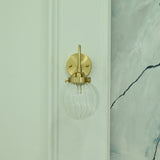 Austin single-light wall sconce featuring a brass finish, curved arm, and clear ribbed glass globe shade, shown from the front with light off.