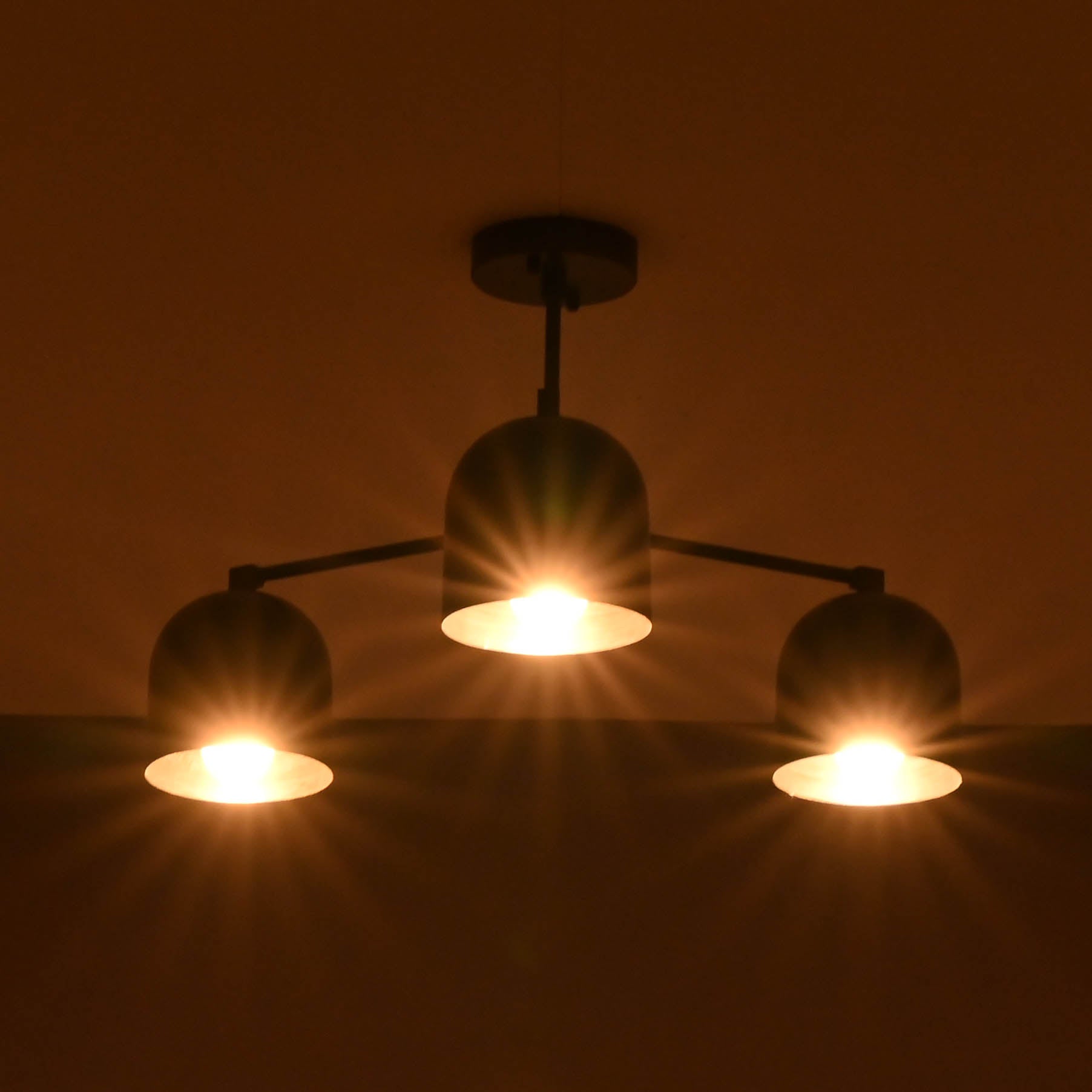 Warm glowing 3-light black brass chandelier with dome-shaped shades, creating a soft ambient effect in a dark room.