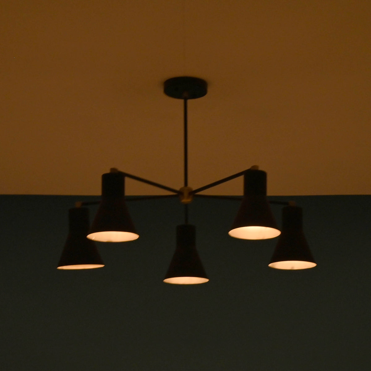 Elegant black brass chandelier with five cone shades, softly lit in a dark room, giving a warm and intimate atmosphere.