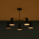 Elegant black brass chandelier with five cone shades, softly lit in a dark room, giving a warm and intimate atmosphere.