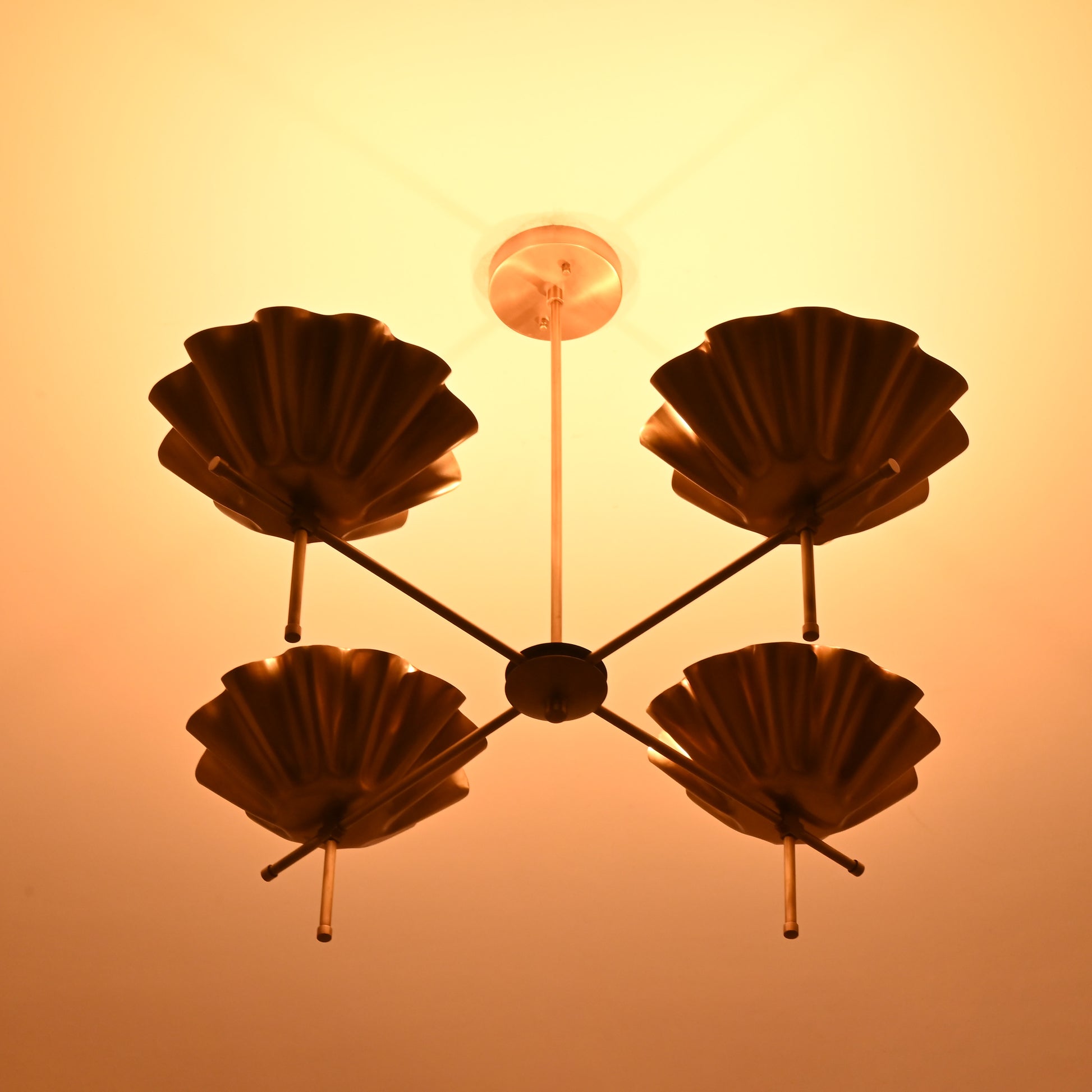 Brass bloom chandelier casting a radiant golden glow on the ceiling in a darkened room.
