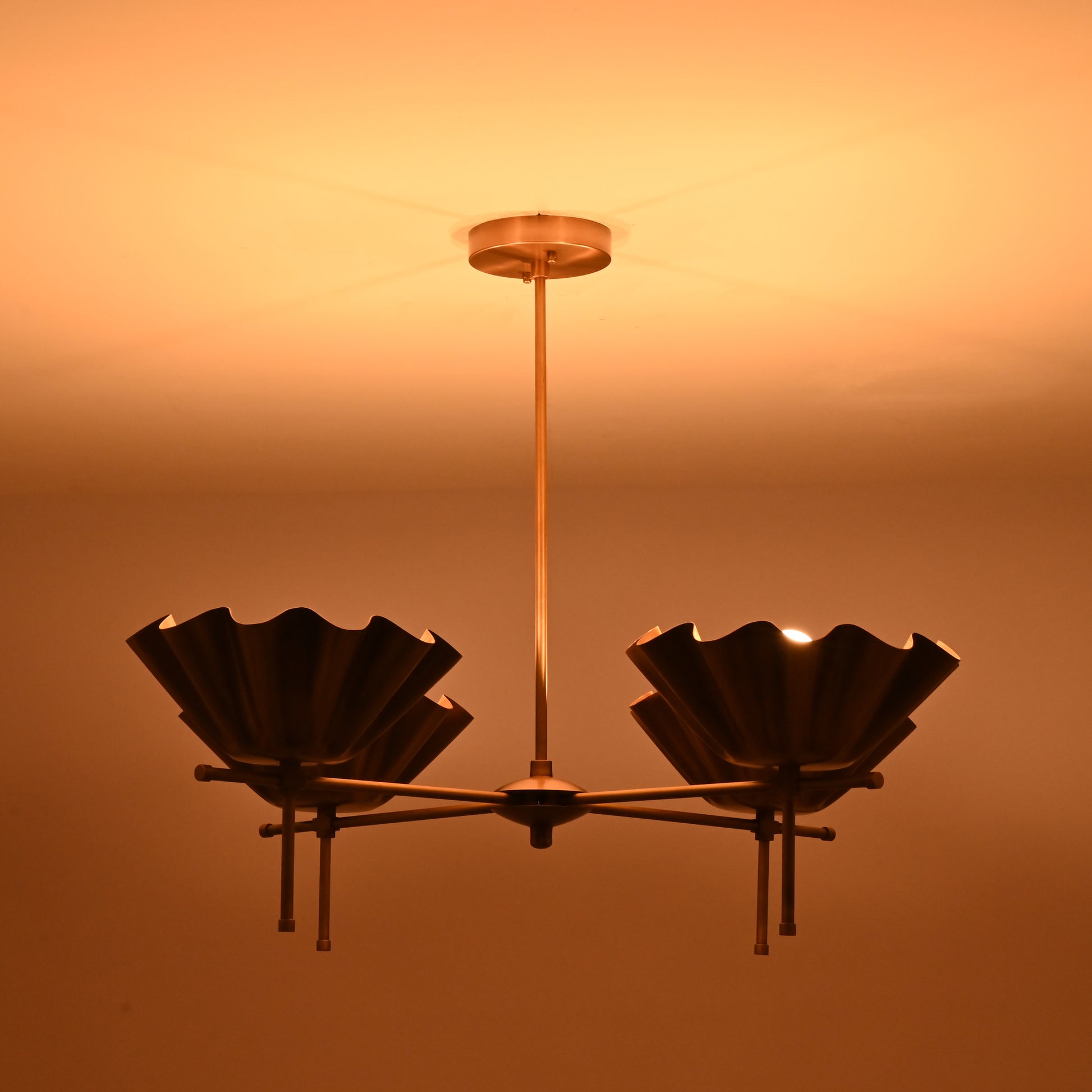 Brass bloom chandelier glowing warmly in a dim room, casting soft ambient lighting on the ceiling.