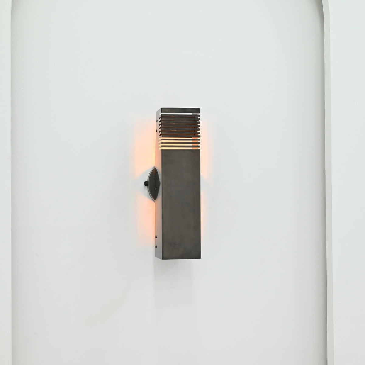 Angled view of Boston 2-light modern rectangular wall sconce with dark metal finish, decorative slatted openings, and soft warm light against a white wall.