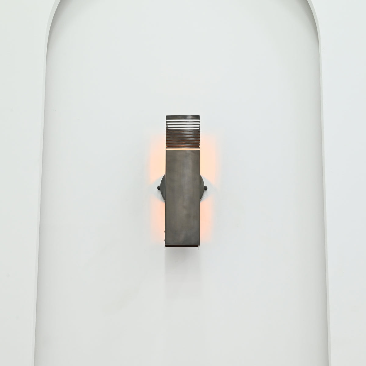 Front view of Boston 2-light dark metal wall sconce mounted inside a white arched niche, featuring horizontal slatted detailing and warm ambient lighting.