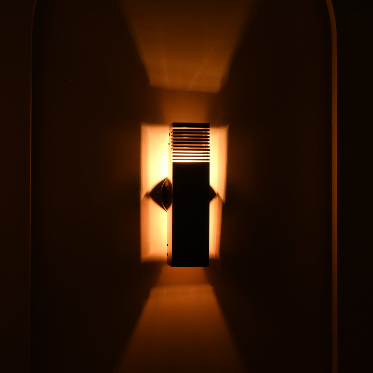 Close-up night view of Boston 2-light dark metal wall sconce showing glowing horizontal slats and dramatic warm up-and-down wall illumination.