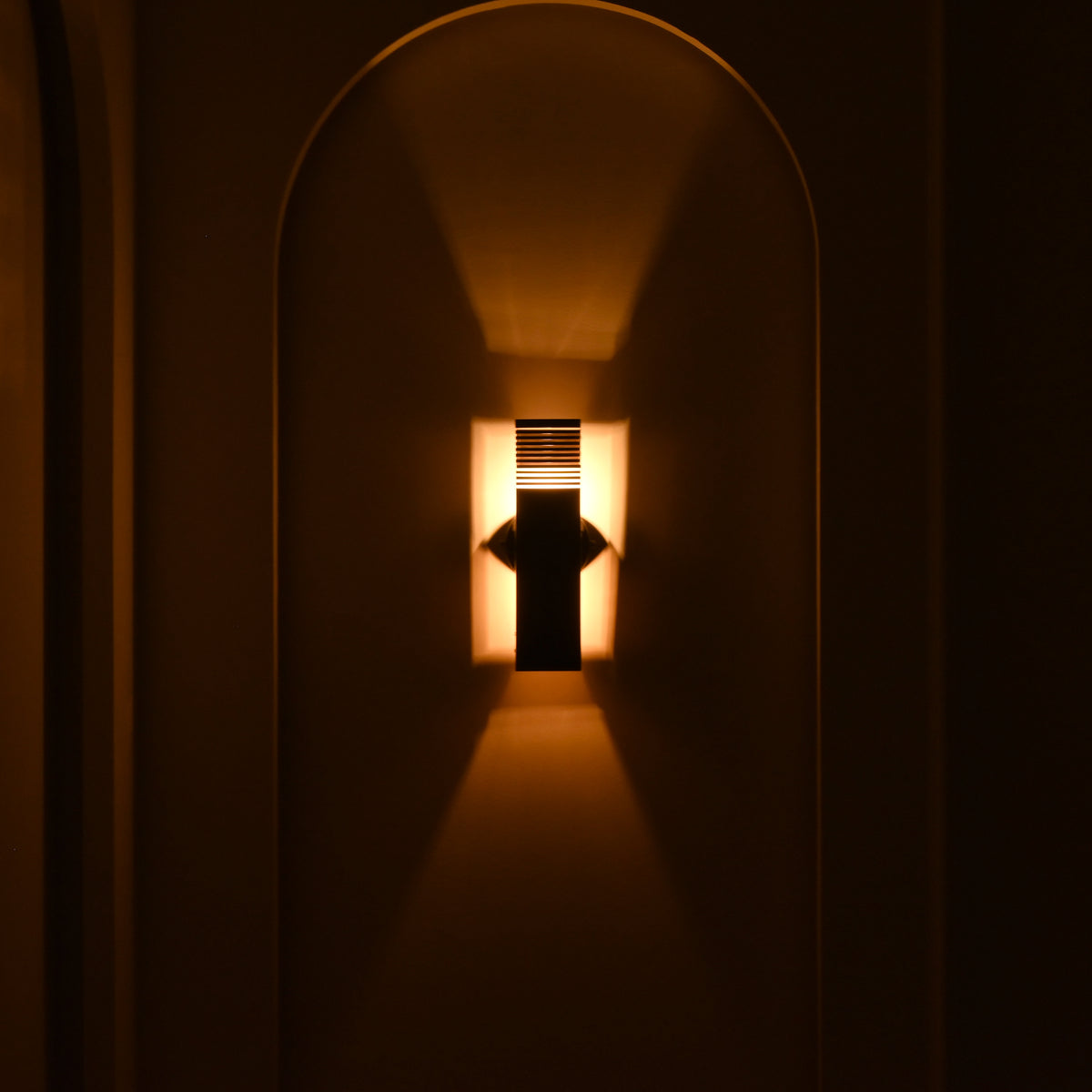  Boston 2-light architectural wall sconce illuminated at night, creating dramatic warm light patterns above and below its dark rectangular metal body.