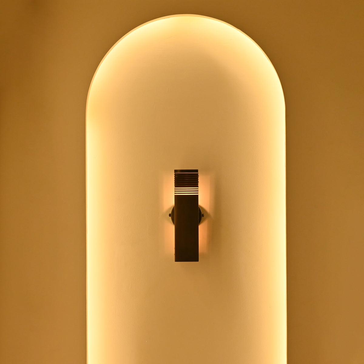 Boston 2-light modern dark metal wall sconce glowing warmly inside a softly illuminated arched niche, creating an elegant evening atmosphere.
