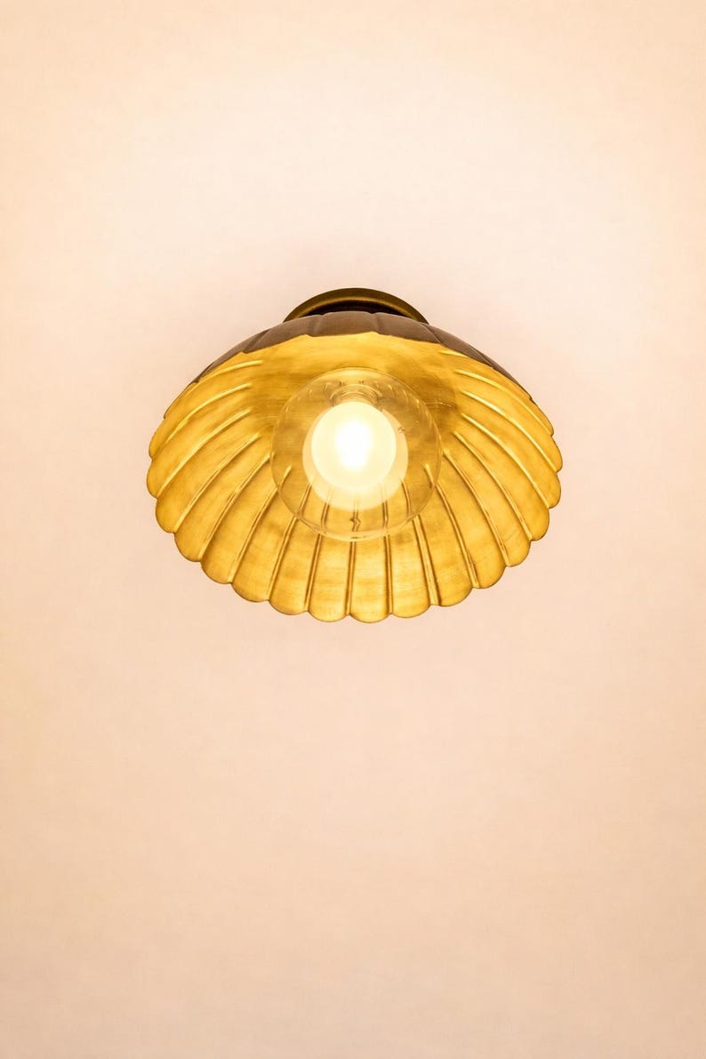 Bottom view of scalloped brass flush mount ceiling light illuminated, showing warm golden reflection inside the bowl shade.