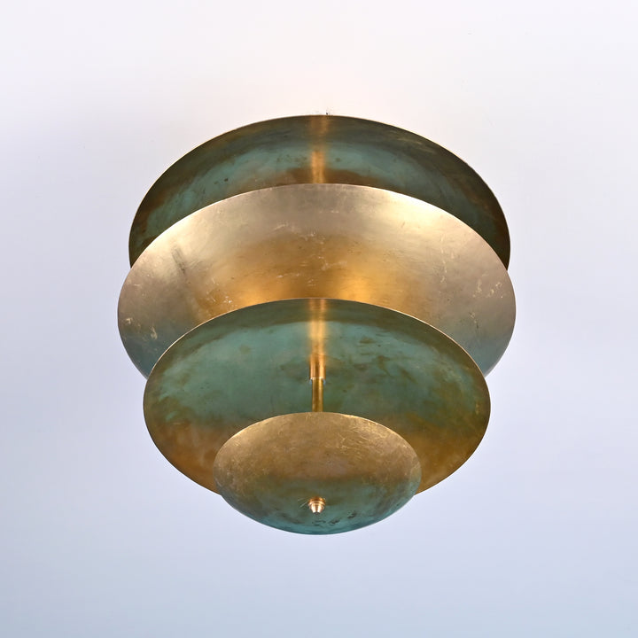 Close-up of handmade layered brass disc chandelier viewed from below, showcasing the patinated green and gold finish in circular tiers