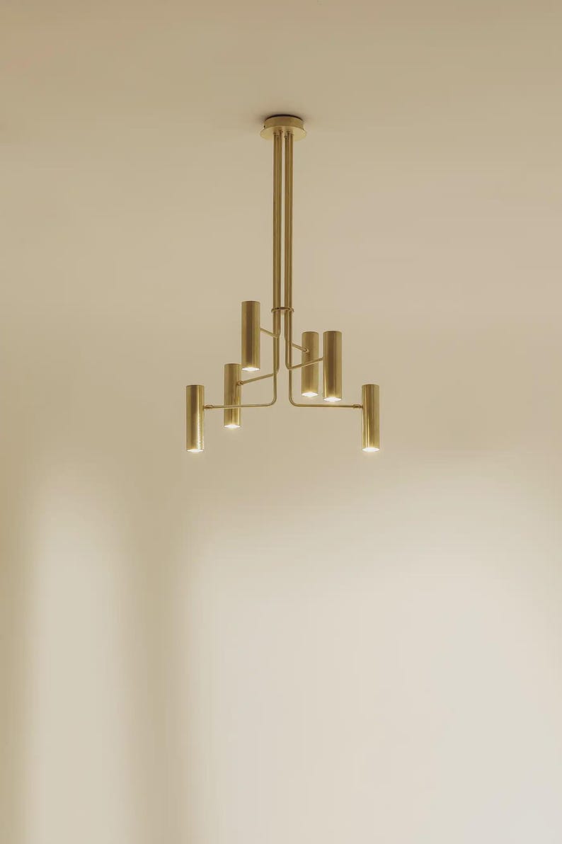 Sculptural brass chandelier with six cylindrical shades and architectural arms, handcrafted in solid brass by Brass Leaf Studio.