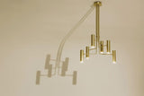 Modern brass chandelier casting artistic shadows on wall, highlighting sculptural form and architectural presence.