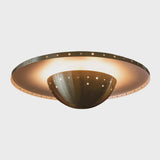 Underside view of brass disc flushmount ceiling light highlighting perforated bowl shade and ambient indirect lighting.