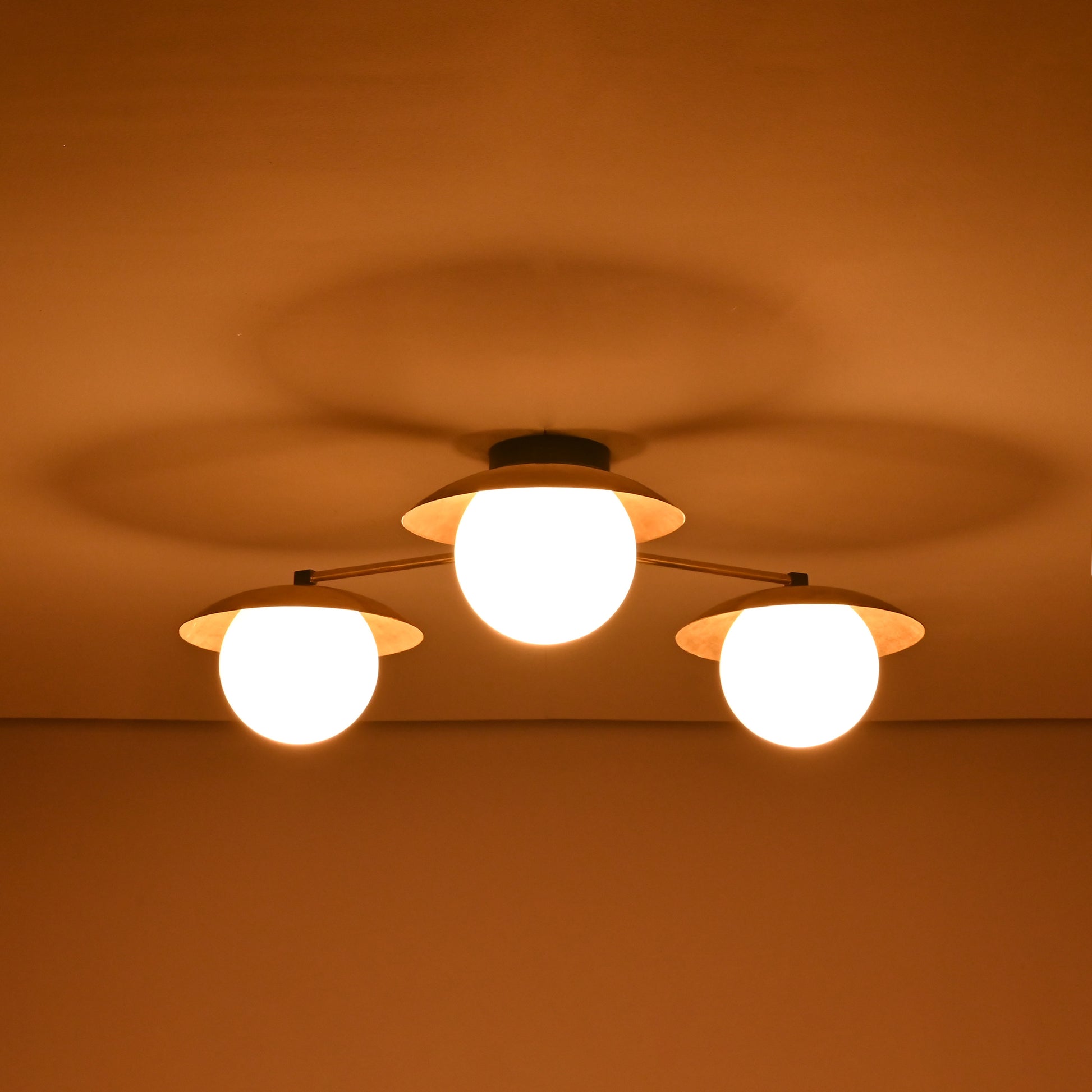 Brass chandelier with three frosted globe shades glowing warmly in the dark, providing cozy ambient light for bedrooms and living areas.