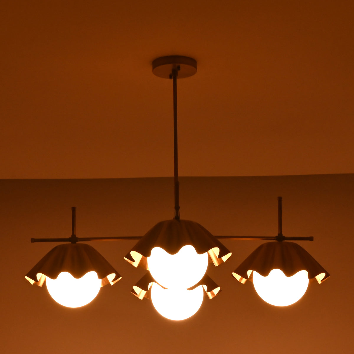 Handmade brass chandelier with three ruffled shades glowing warmly in the dark, offering ambient lighting and sculptural design.