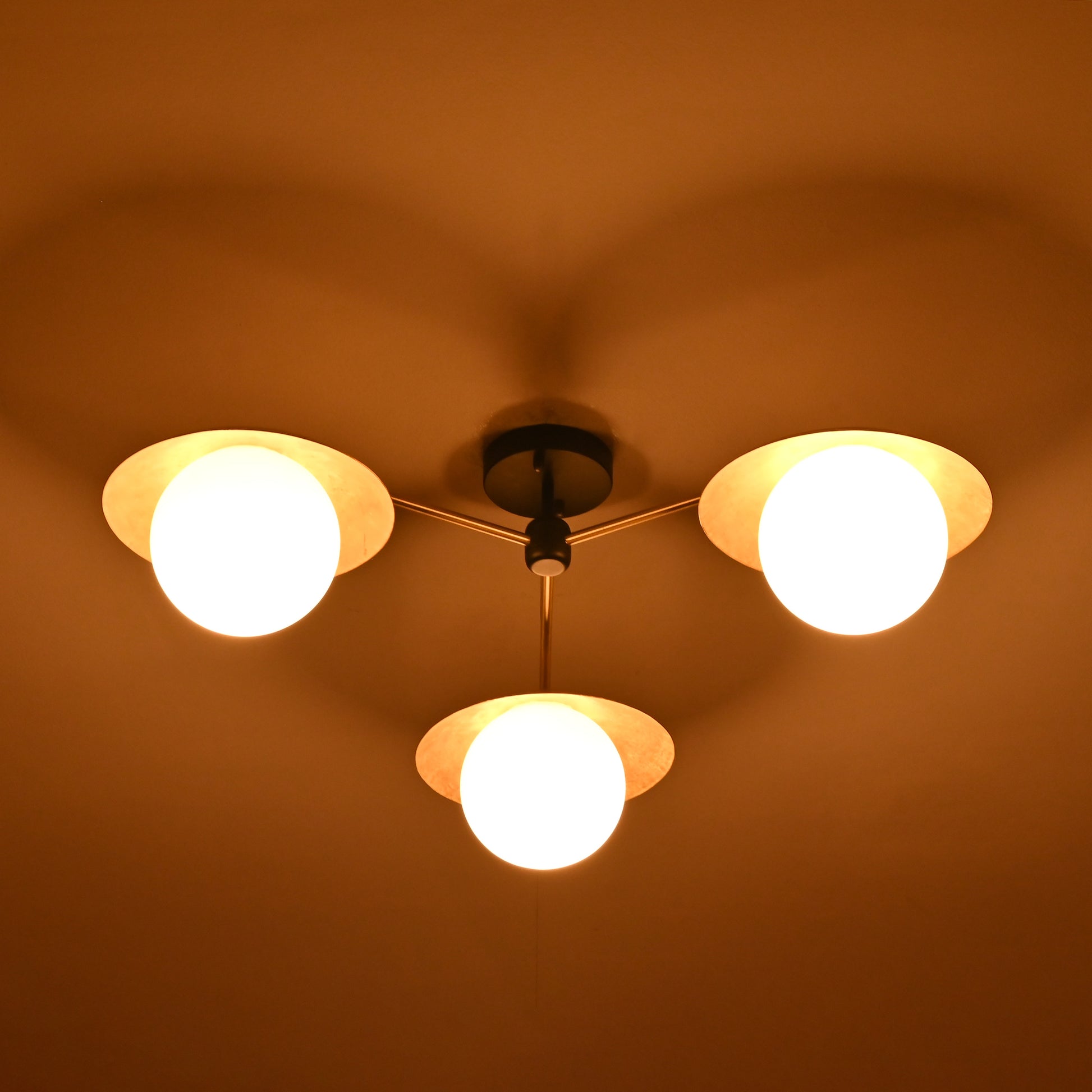 Brass chandelier with three frosted globes and disc shades glowing warmly at night, creating ambient lighting for cozy living spaces.
