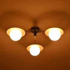 Brass chandelier with three frosted globes and disc shades glowing warmly at night, creating ambient lighting for cozy living spaces.