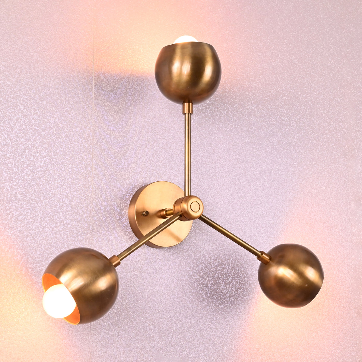 Angled view of brass flush mount ceiling lamp with three spherical shades in brushed brass finish, unlit against neutral background.