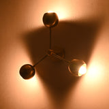 Side angle of brass flush mount chandelier with three spherical shades emitting warm ambient light on the wall.