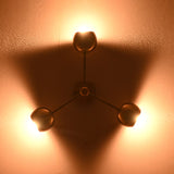 Ambient view of brass flush mount ceiling light with three glowing spherical shades casting triangular light patterns on the wall.
