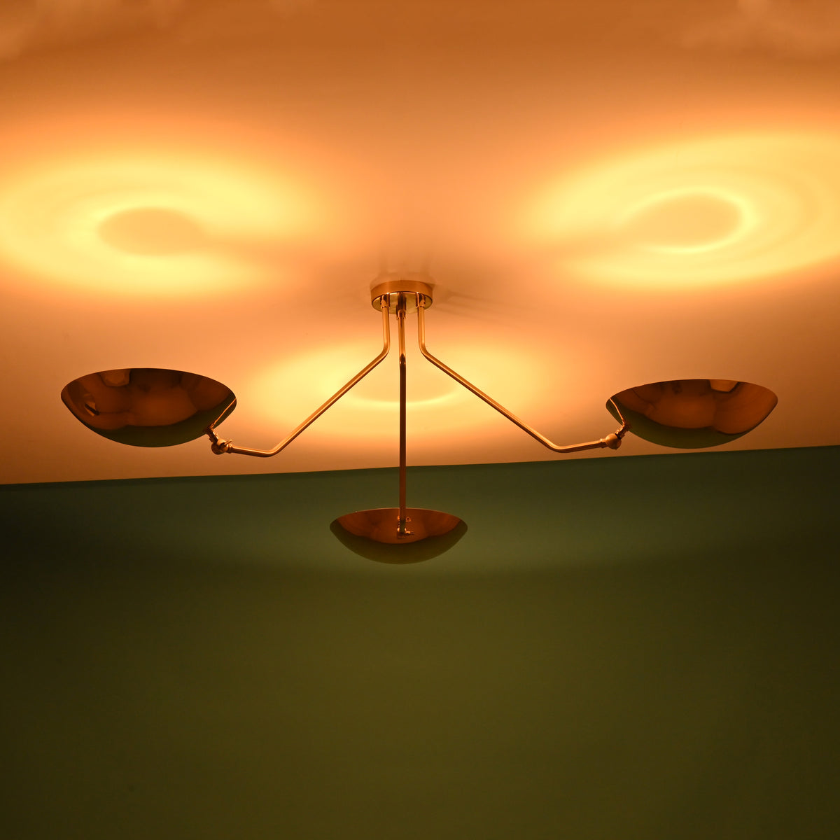 Brass flushmount chandelier casting circular warm glows on the ceiling, featuring three brushed brass bowl-shaped shades.