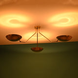 Brass flushmount chandelier casting circular warm glows on the ceiling, featuring three brushed brass bowl-shaped shades.