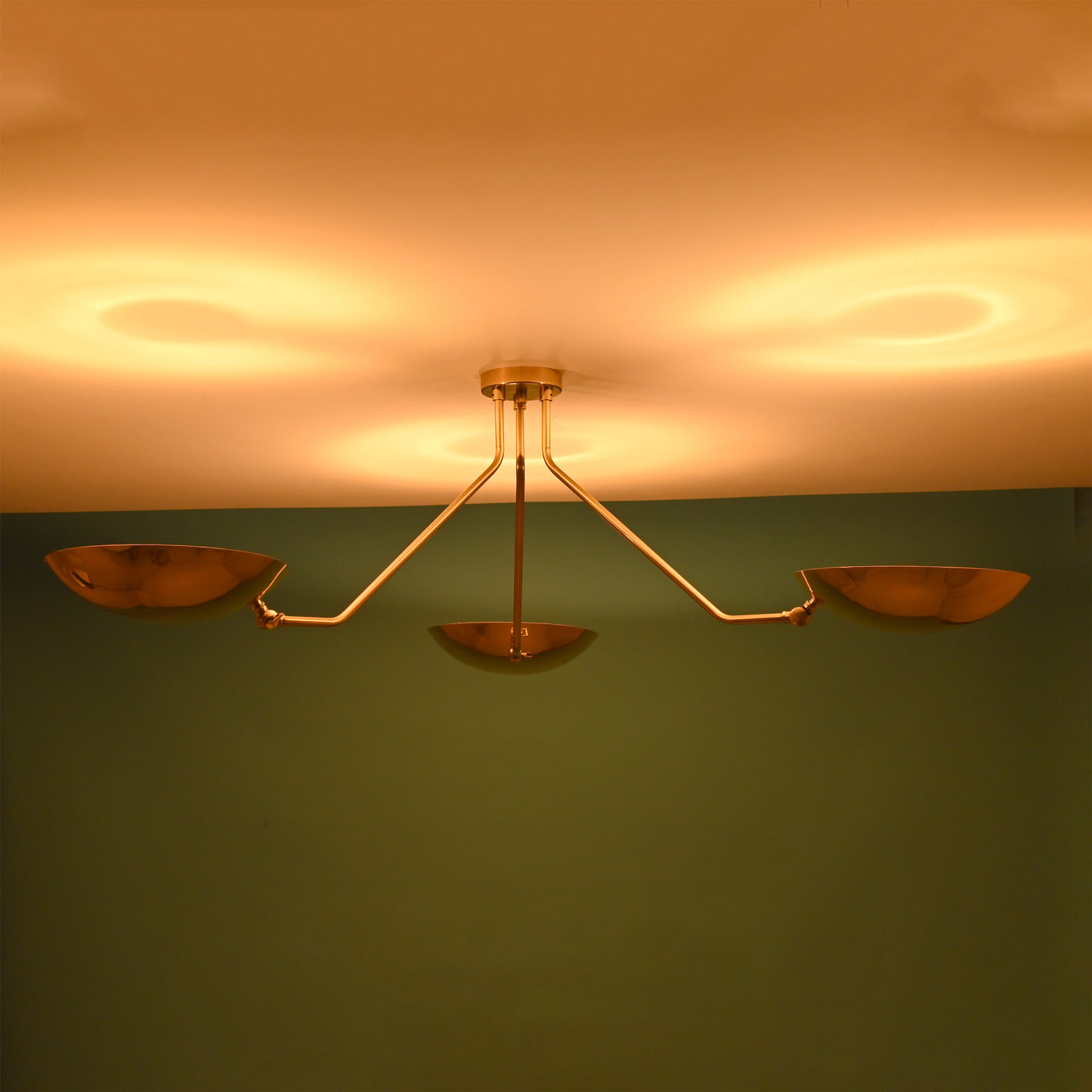 Warm-lit brass flushmount chandelier with three bowl-shaped shades casting soft ambient reflections on the ceiling.
