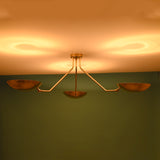 Warm-lit brass flushmount chandelier with three bowl-shaped shades casting soft ambient reflections on the ceiling.