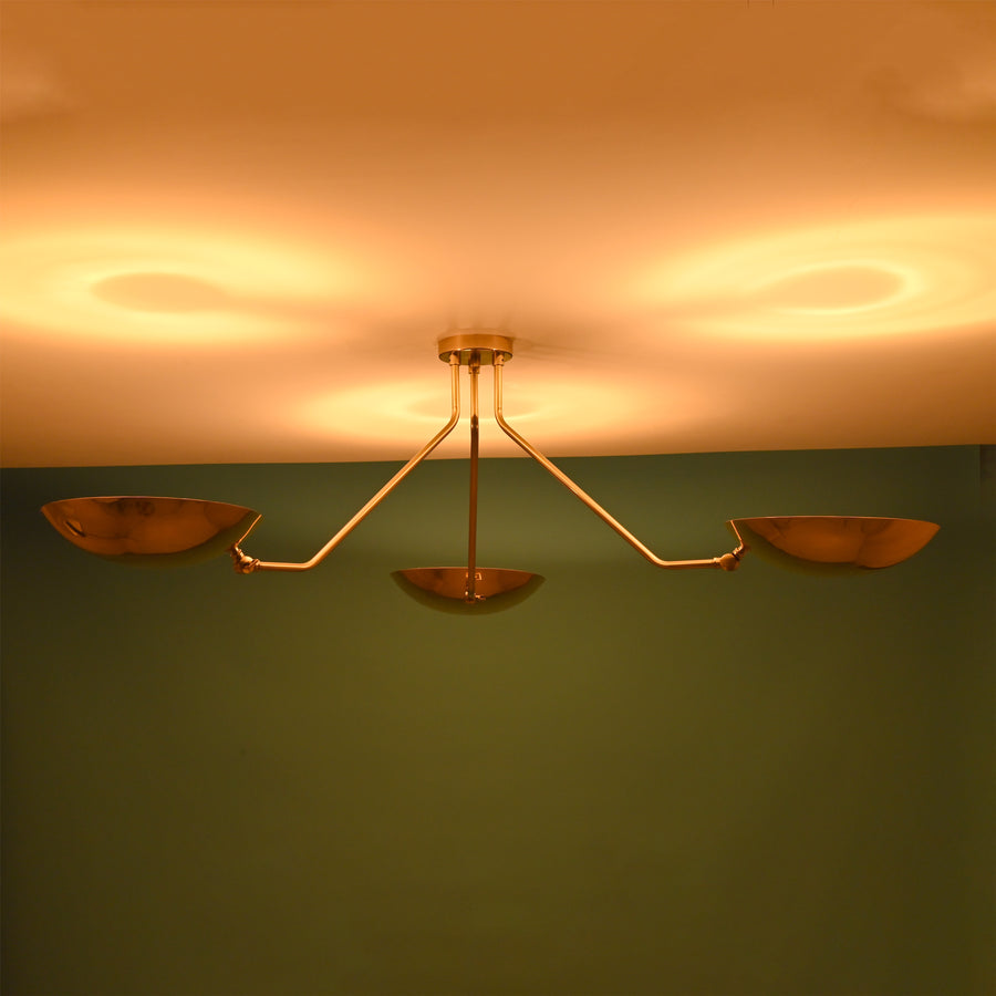 Warm-lit brass flushmount chandelier with three bowl-shaped shades casting soft ambient reflections on the ceiling.