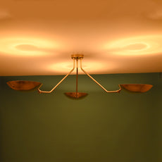 Warm-lit brass flushmount chandelier with three bowl-shaped shades casting soft ambient reflections on the ceiling.