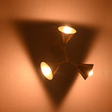 Brass three-shade wall sconce lit in a dark room, producing a warm triangular shadow and soft ambient glow.